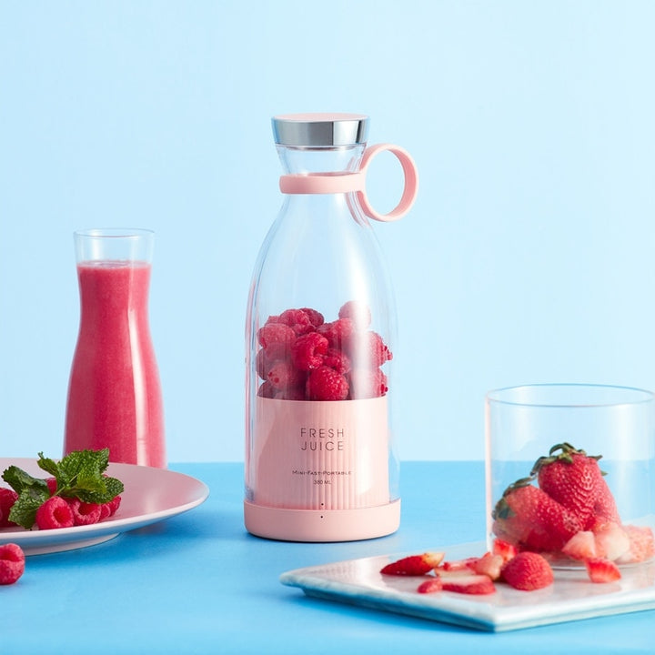 Pink portable blender with fresh raspberries, glass with blended drink, glass with fresh strawberries